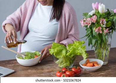 Cropped View Of Pregnant Woman Pouring Olive Oil Into Salad At Kitchen