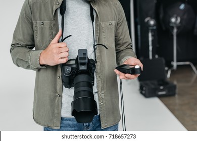 cropped view of professional male photographer with digital photo camera and light meter in photo studio