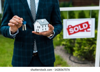 Cropped View Of Realtor Holding Carton House Model And Keys Near Board With Sold Letters 