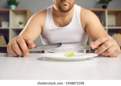 Cropped View Sad Unhappy Man On Diet Sitting At Table Holding Cutlery Near Plate With Tiny Little Apple Fruit Piece For Lunch. Strict Dieting Special Program Eating Less Food For Slimming, Lose Weight