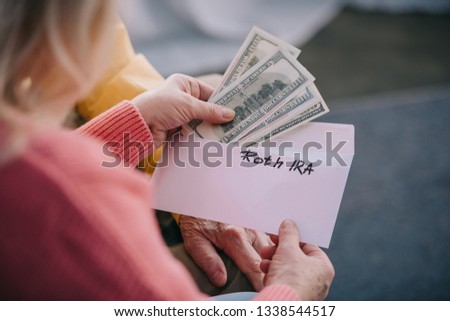 cropped view of senior couple holding envelope with 'roth ira' lettering and dollar banknotes