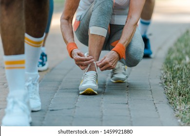 cropped view of senior woman sitting and tying shoelaces in park  - Powered by Shutterstock