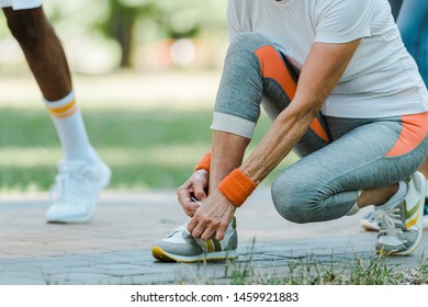 cropped view of senior woman sitting and tying shoelaces in park  - Powered by Shutterstock