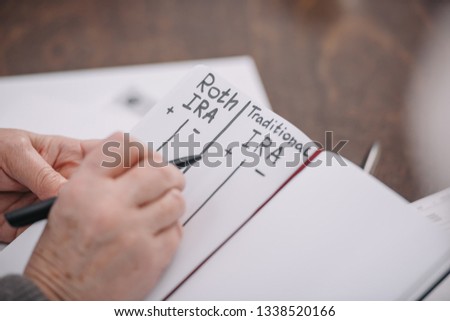 cropped view of senior woman writing in notebook with roth ira and traditional ira words