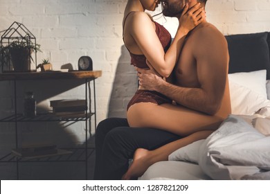 cropped view of sexy couple passionately embracing on bed at home