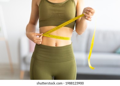 Cropped view of slim Indian woman measuring her waist with tape measure at home, closeup. Unrecognizable Asian lady checking result of weight loss diet or liposuction indoors