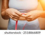 Cropped view of slim woman measuring waist with tape measure at home, close up. European woman checking the result of diet for weight loss or liposuction indoors