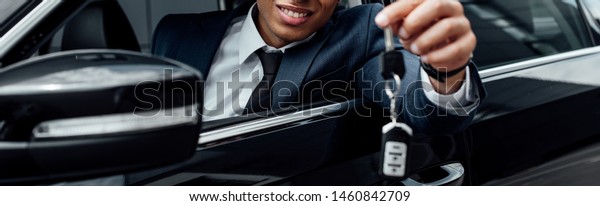 cropped view of smiling african american\
businessman holding car key, panoramic\
shot