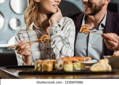 Cropped view of smiling happy couple eating sushi in restaurant