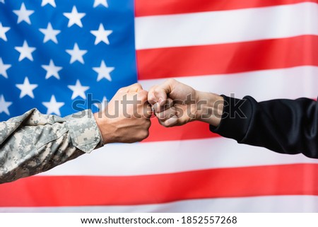 cropped view of soldier fist bumping with civilian man near american flag on blurred background