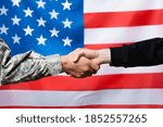 cropped view of soldier shaking hand with civilian man near american flag on blurred background