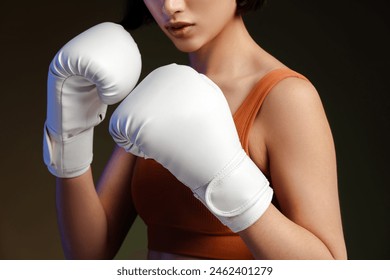 Cropped view of strong woman wearing white boxing gloves, standing isolated on black background. Female training, motivation, lifestyle