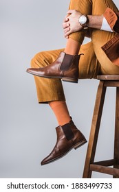 Cropped view of stylish man in brown shoes sitting on wooden chair isolated on grey 