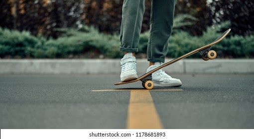 Cropped view of a stylish man in white sneakers and green pants with a skateboard, on a yellow crosswalk. - Powered by Shutterstock