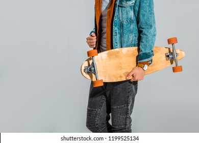 cropped view of stylish skateboarder holding longboard isolated on grey