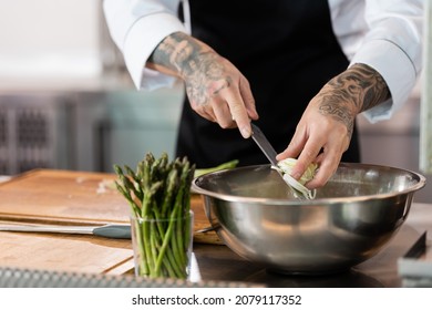 Cropped View Of Tattooed Chef Holding Knife And Sliced Leek In Kitchen