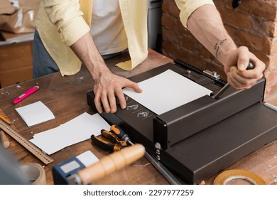 cropped view of tattooed man using paper trimmer machine in modern print center