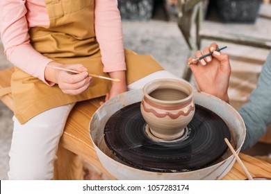 cropped view of teacher and kid painting ceramic pot on pottery wheel in workshop - Powered by Shutterstock