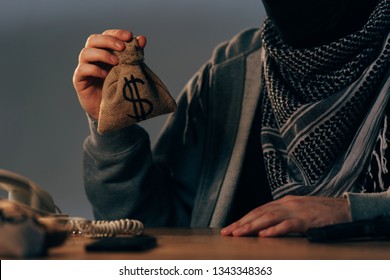 Cropped View Of Terrorist In Keffiyeh Scarf Holding Small Money Bag With Dollar Sign