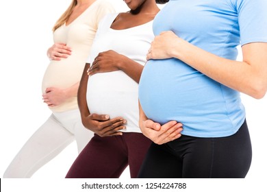 cropped view of three pregnant women holding hands on bellies isolated on white
