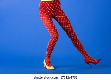 cropped view of trendy model in fishnet tights, yellow and red heels posing on blue