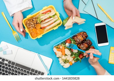 Cropped View Of Two Women Holding Forks Over Lunch Boxes With Food Near Laptop