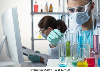 Cropped view of two young scientists in protective equipment in a laboratory. A man looking at beakers, a woman working with data in a computer. Selected focus on on male hand - Powered by Shutterstock