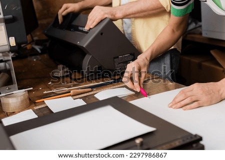 cropped view of typographer cutting paper with knife near colleague in print center