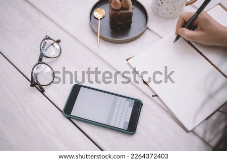 Cropped view of unrecognizable female designer with fineliner drawing in sketchbook at cafeteria table with optical eyeglasses and blank smartphone technology with copy space area, style concept