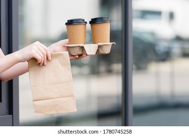 Cropped View Of Waitress Holding Paper Bag And Coffee To Go Near Cafe On Urban Street