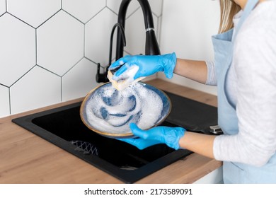 Cropped view of woman in apron and gloves washing plates. Kitchenware cleaning in sink faucet in modern kitchen. Housewife concept. Cleaning service worker - Shutterstock ID 2173589091