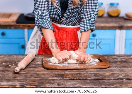 cropped view of woman in apron kneading dough in kitchen