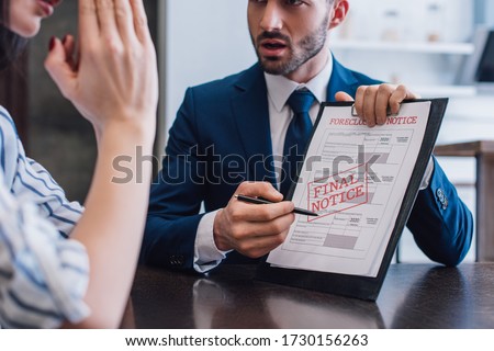 Cropped view of woman and collector pointing with pen at documents with foreclosure and final notice lettering at table