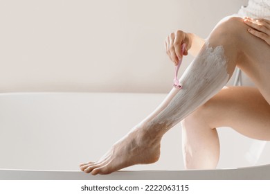 Cropped view of woman depilating shins over ceramic bathtub. Female shaved leg with pink plastic razor. Lady using epilation gel foam for sensitive skin. Pampering, moisturizing, self care in bathroom - Powered by Shutterstock