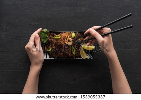 cropped view of woman eating delicious spicy thai noodles with chopsticks on wooden grey surface