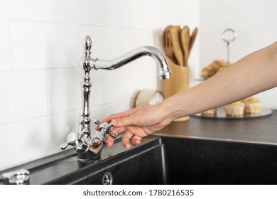 Cropped View Of Woman Hand Closed Or Open Water In Faucet Over Black Sink, Against White Tiled Wall. Element Of New Kitchen In Modern Apartment