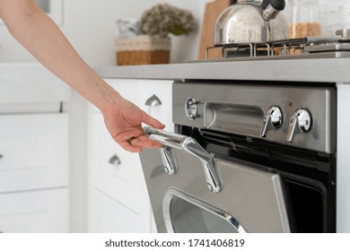 Cropped View Of Woman Hand Open Door At Modern Silver Gas Oven. Fragment Of New Kitchen With Modern Interior And Built In Cooking Appliance