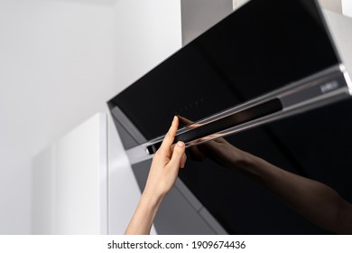 Cropped view of woman hand turning on modern electric cooker hood standing on contemporary kitchen with built in appliance and copy space white wall on background