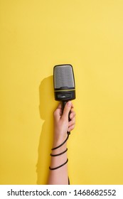 cropped view of woman holding microphone on yellow background 