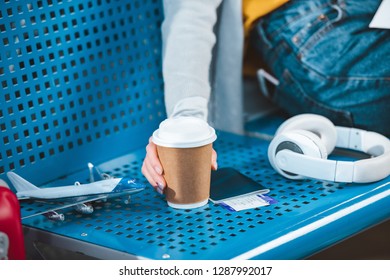 cropped view of woman holding paper cup near plane model and headphones
