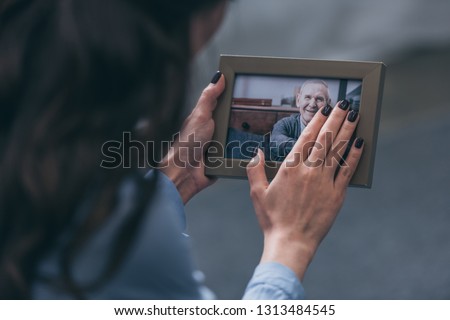 cropped view of woman holding photo frame with mature man at home, grieving disorder concept