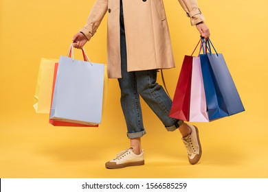 Cropped view of woman holding shopping bags in hands on yellow background
