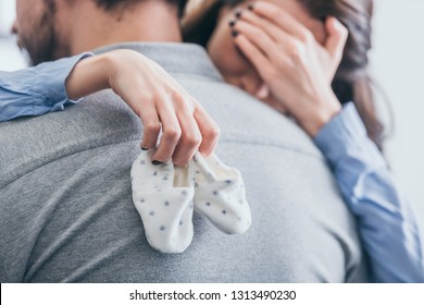 Cropped View Of Woman, Hugging Man, Holding Baby Socks And Crying In Room, Grieving Disorder Concept