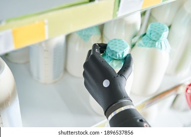 Cropped View Of The Woman Implant Hand Taking Bottle Of Milk From Shelf In Dairy Department Store. Customer Buying Milk While Filling And Stocking Shelves. Woman Choosing Food Products