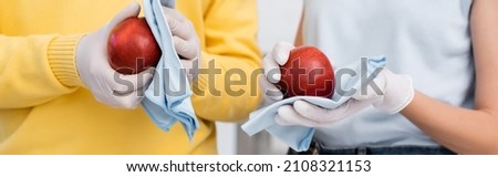 Cropped view of woman in latex gloves cleaning apple with rag near boyfriend at home, banner