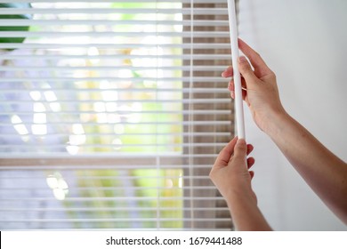 Cropped view of woman making lighting range control, opened modern white louvers on windows in bright room