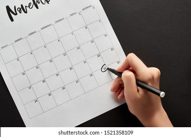 cropped view of woman marking black Friday date in calendar on black background