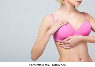 cropped view of woman in pink bra touching breast isolated on grey, breast cancer concept