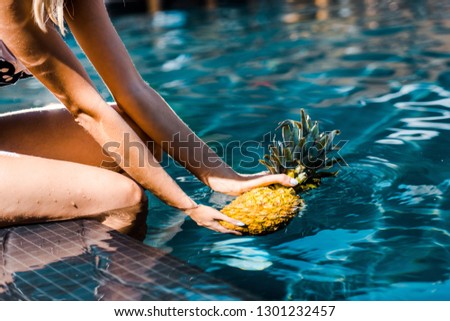cropped view of woman posing with sweet pineapple near swimming pool