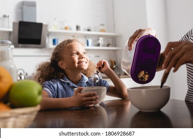 cropped view of woman pouring cornflakes into bowl near excited african american girl